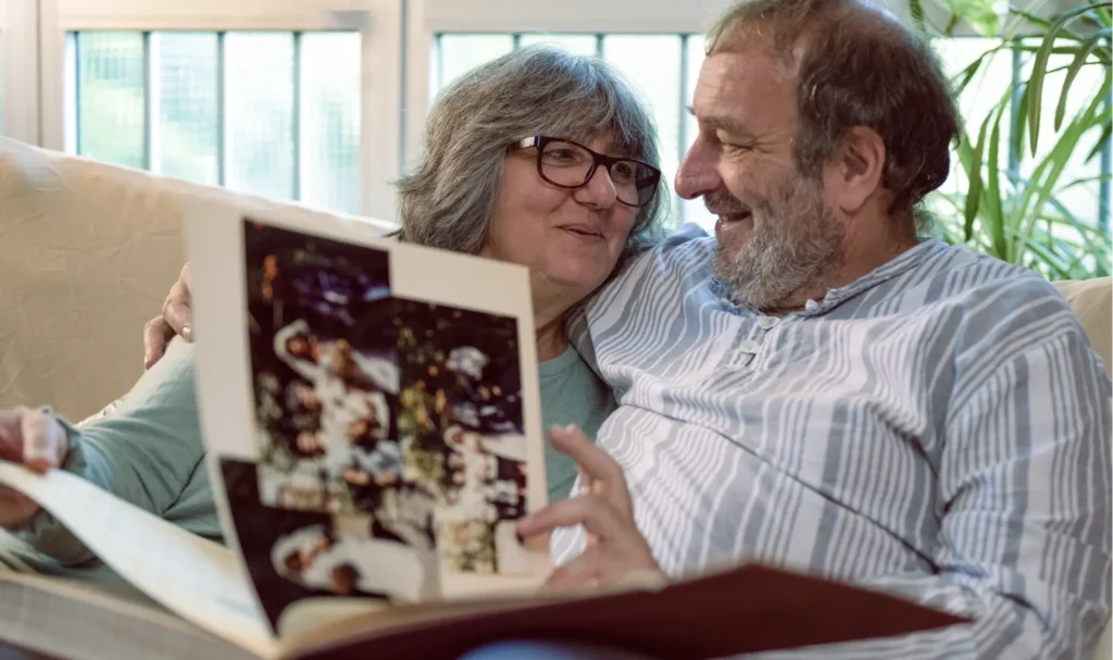 An elderly couple reviewing a family history book, showing photos from their wedding many years ago