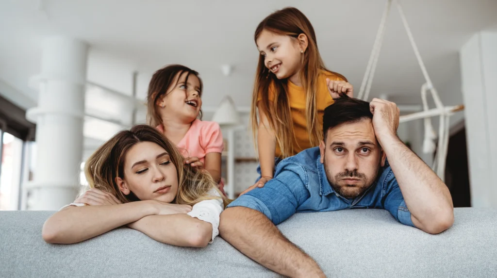 Two parents looking stressed and burnt out with their energetic children behind them. 