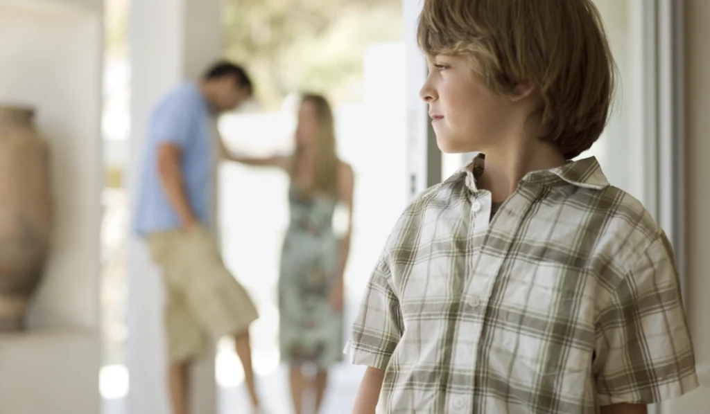 A boy looking a little upset with his parents having a difficult conversation in the background