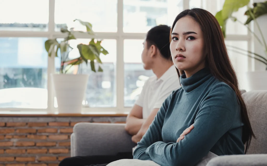 A lady looks upset as she has sat on a sofa, turning away from her partner.