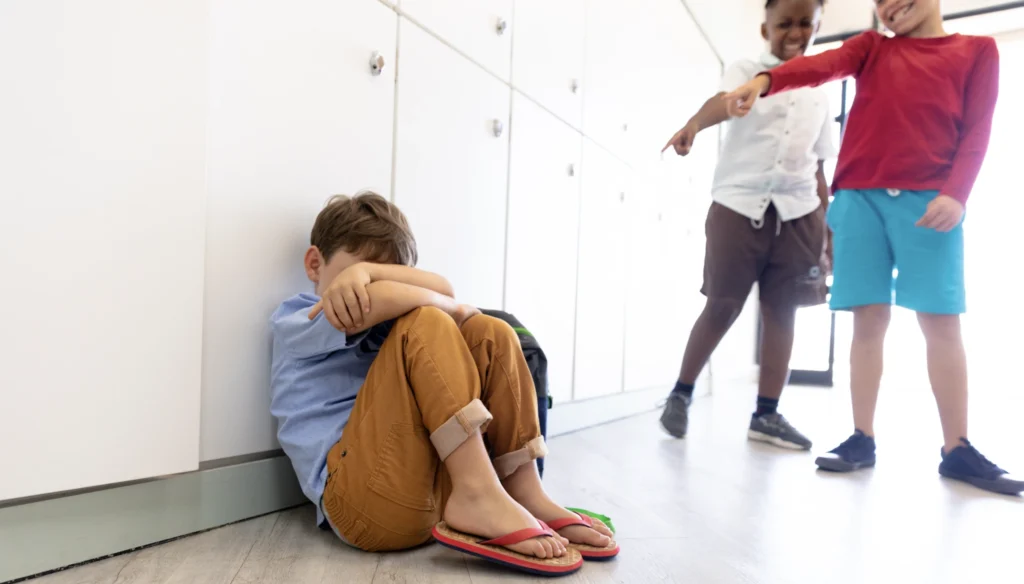 Two boys excluding a third and pointing their fingers at him.