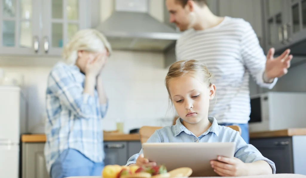Two upset parents arguing with their daughter looks sad and plays on her tablet.