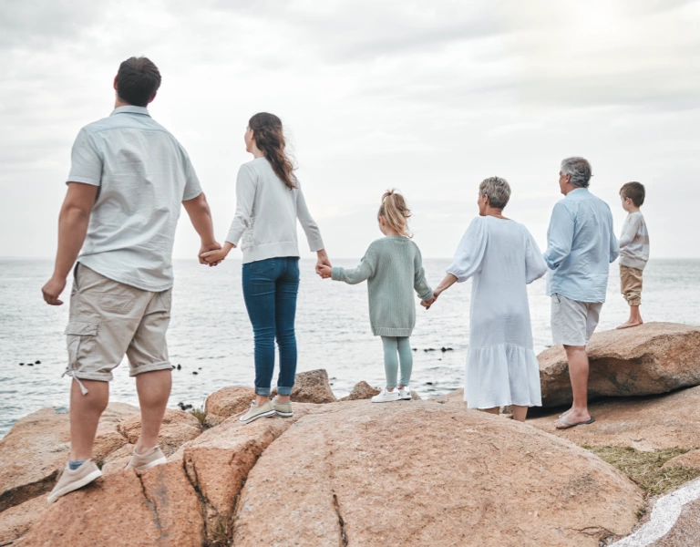A large multi-generational family stood together on a beach, looking out to sea.