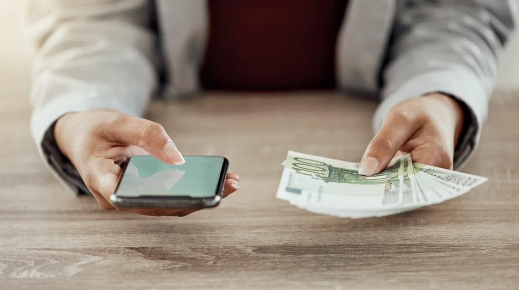 A lady holding a phone with an app open in one hand and money in the other hand. 