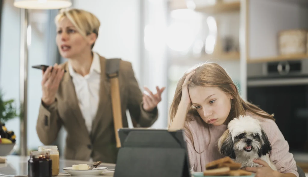 A mother stressed on her phone while her child looks bored on her tablet