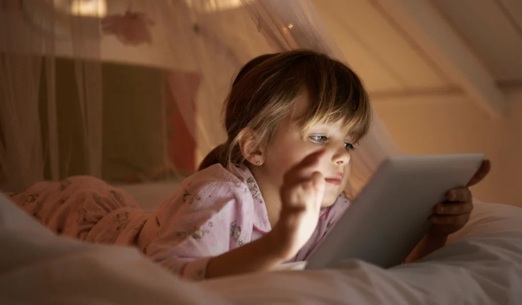 A little girl staying up at night, looking at her tablet instead of sleeping. 