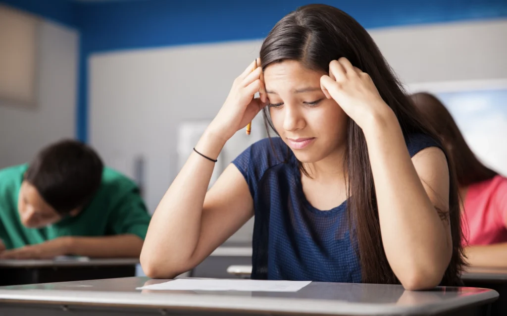 A stressed teenage girl holding her head in her hands during an exam 