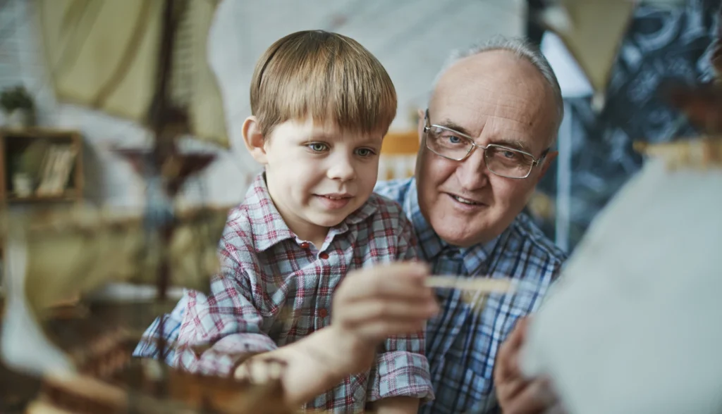 A grandfather and grandson building a model ship together, illustrating the value of respect for elders and intergenerational connection.