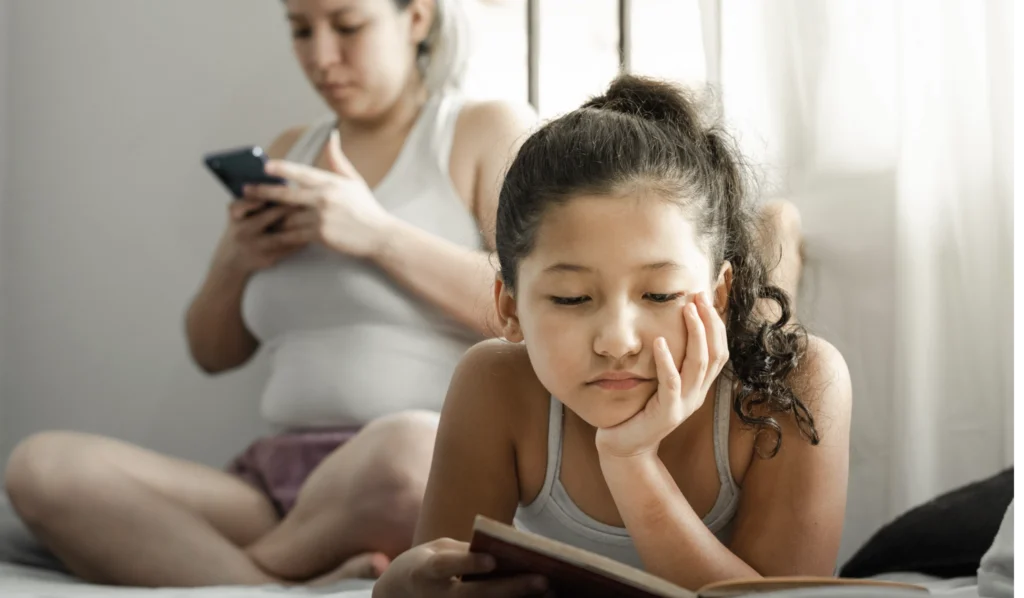 A mother ignores her child as she focuses on her smartphone. 