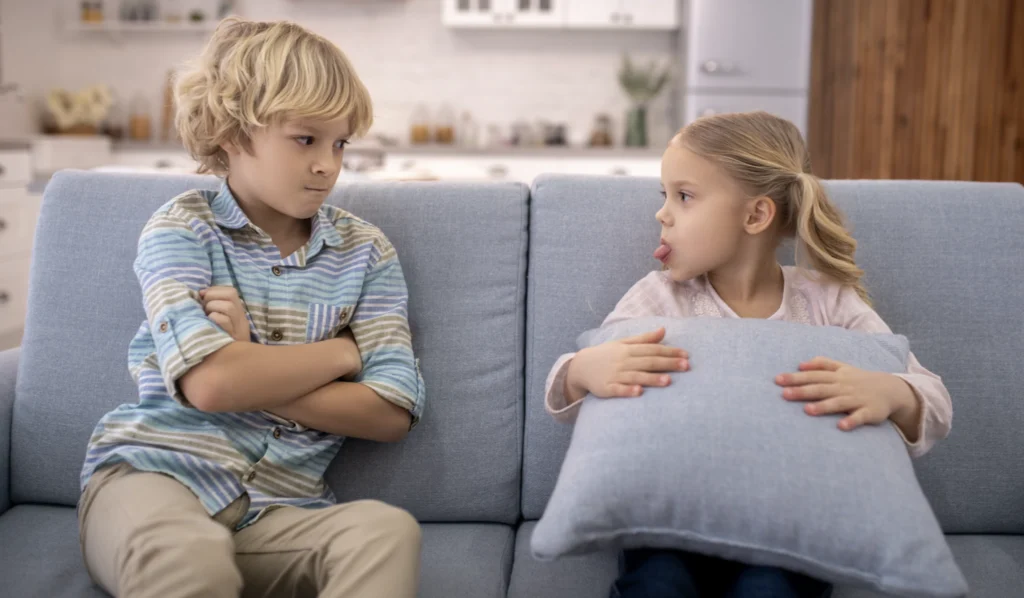 Two young siblings on a sofa, visibly annoyed at each other. 