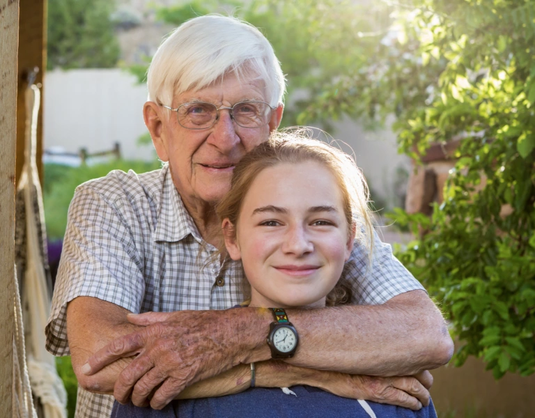 A grandfather and granddaughter embracing and looking happy